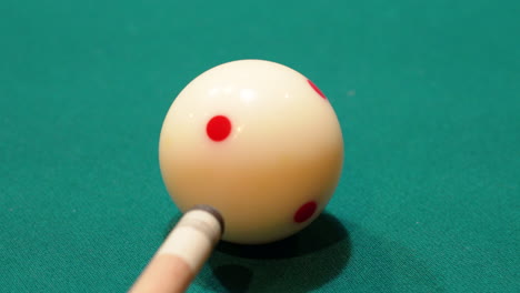 primer plano de billar de una bola blanca con manchas rojas que se dispara rápidamente en una mesa de billar con la punta de un palo de madera que se cierne sobre el fieltro verde después de varios golpes de práctica, sin rostros