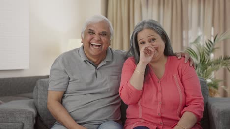 Happy-Indian-old-couple-laughing-while-watching-TV