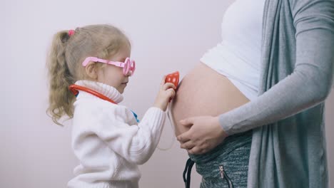 una niña toca el vientre de su mamá embarazada con un estetoscopio de juguete