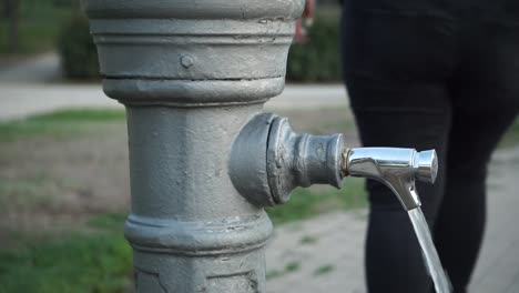 Frau-Schaltet-Den-öffentlichen-Wasserhahn-Im-Park-Ein,-Zeitlupe-Aus-Nächster-Nähe