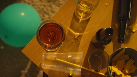 overhead shot of messy table covered with empty wine glasses with beer bottles and snacks after house party 2