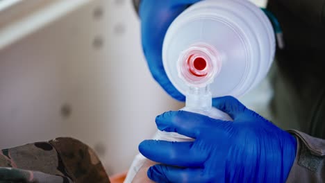cerca un médico militar hombre confiado con guantes de goma azul bombea aire usando una botella blanca mate y realiza respiración artificial en un soldado herido inconsciente en una ambulancia