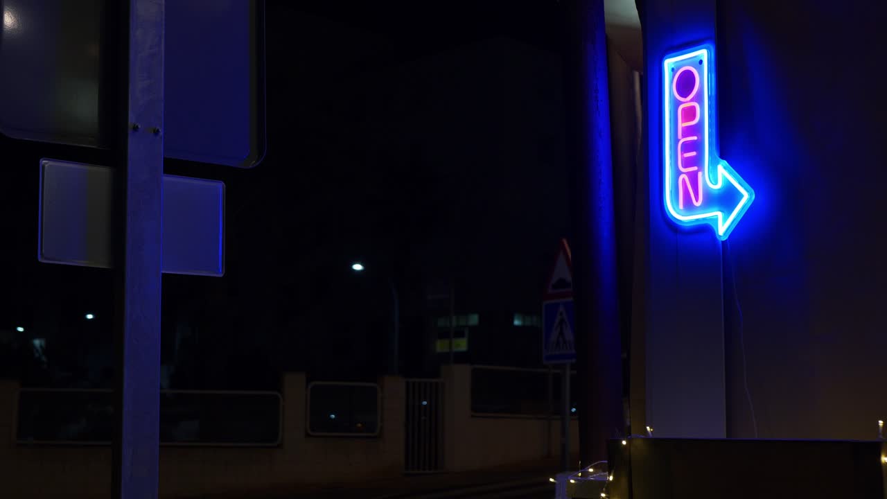 un letrero de neón abierto en una noche oscura con coches pasando