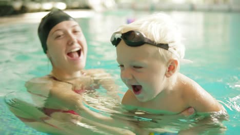 Happy-little-boy-is-swimming-in-the-pool-together-with-his-mother.-She-is-holding-him-and-teaching-how-to-swim.-Happy-family