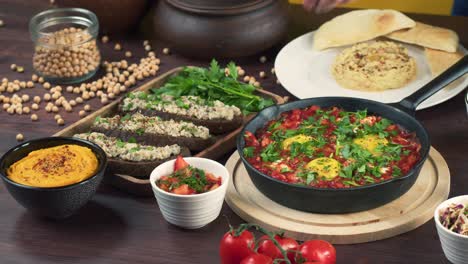 traditional israeli cuisine. putting forshmak on table. shakshuka in pan decorated with parsley, hummus close-up. national jewish dishes. eggs fried in tomato sauce. middle eastern culture