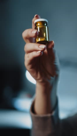 mujer seria con largo cabello blanco en ropa gris toma un pequeño frasco con nuevas pastillas no probadas sentado en una habitación semi-oscura en la luz de atrás vista cercana cámara lenta