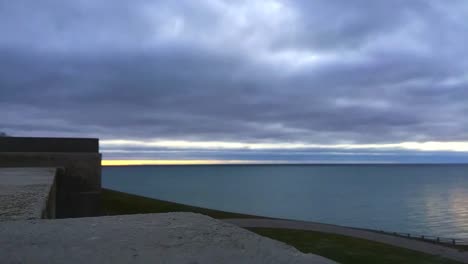 Lapso-De-Tiempo-Temprano-En-La-Mañana-En-El-Lago-Ontario,-Tomado-Desde-La-Muralla-De-La-Cima-De-Una-Colina,-Mostrando-Patrones-De-Olas,-Movimiento-De-Nubes-Y-Gente-Saliendo-A-Caminar