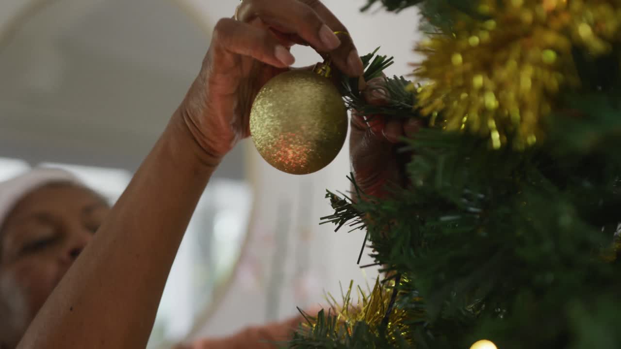 mano de una feliz mujer mayor afroamericana con sombrero de santa decorando el árbol de navidad