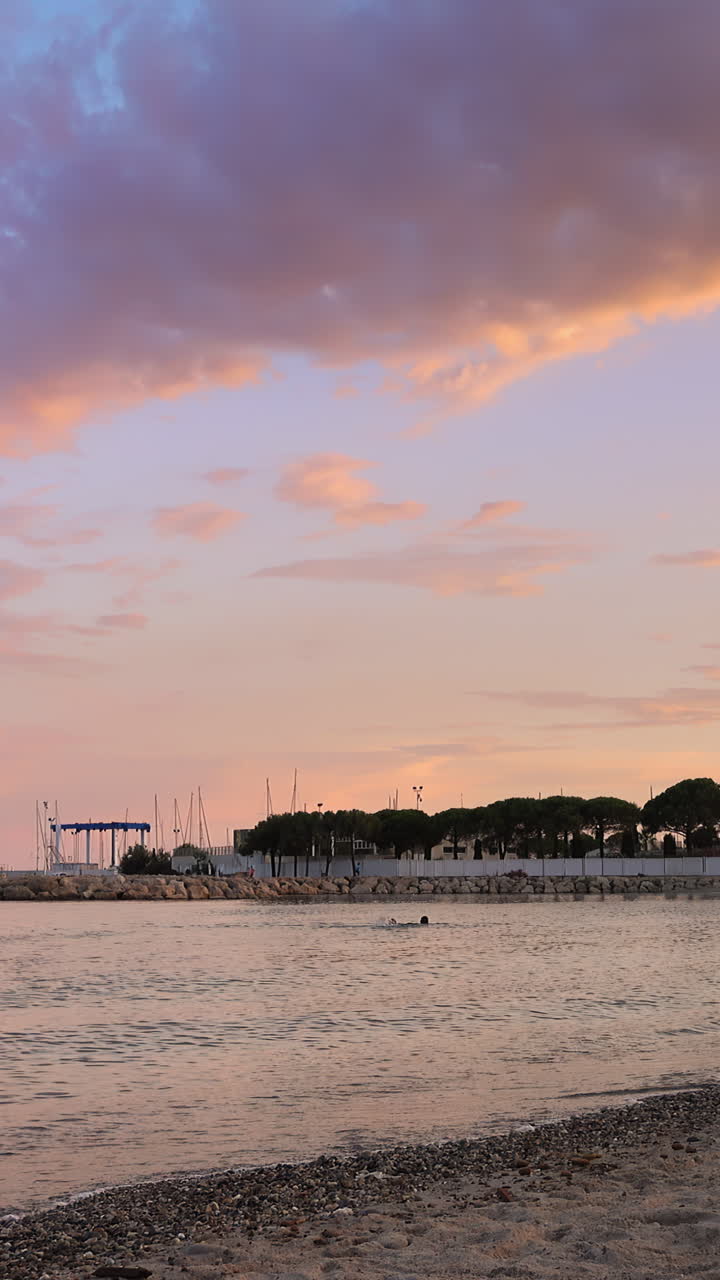People playing and relaxing on the beach at sunset in Cannes, France. Vertical