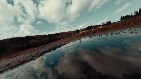 FPV aerial drone flying and gliding over wetlands water and bog marshlands during a cloudy day. The water reflects the sky, clouds and the trees and landscape in the distance. Fast flying forward.
