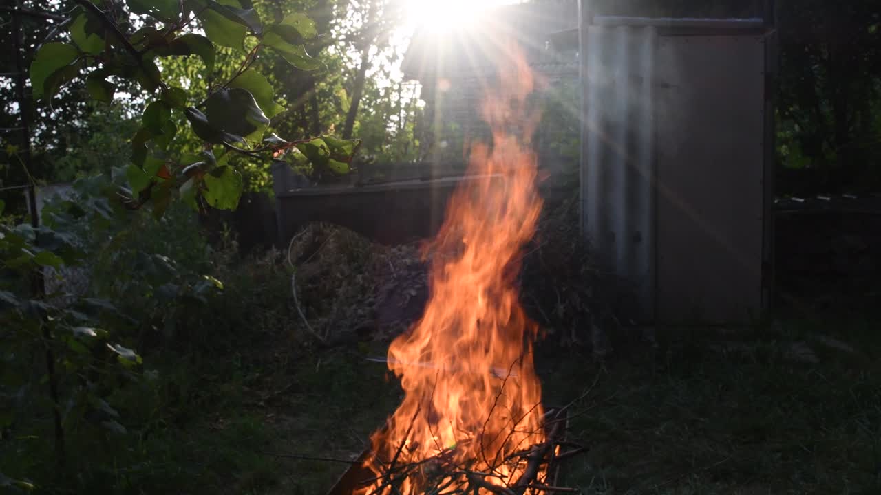 fuego ardiente al aire libre bajo los rayos del sol. llamas de fogata en un fondo rústico borroso