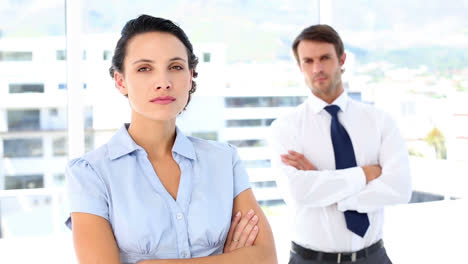 Serious-businesswoman-looking-at-camera-with-colleague-behind-her