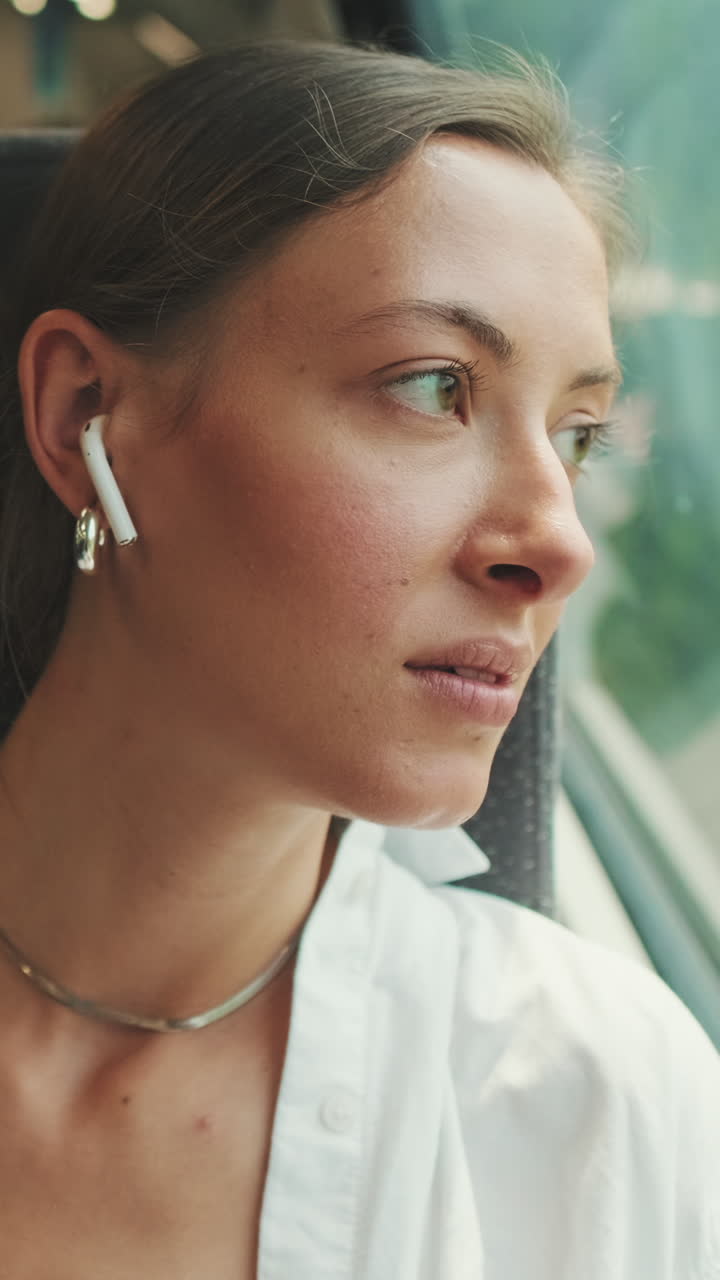 Giovane donna pensierosa che guarda fuori dal finestrino del treno con gli auricolari