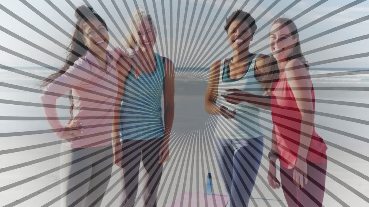 Quattro donne in piedi sulla spiaggia con tappetino da yoga e bottiglia d'acqua, una alza il telefono per iniziare l'allenamento.