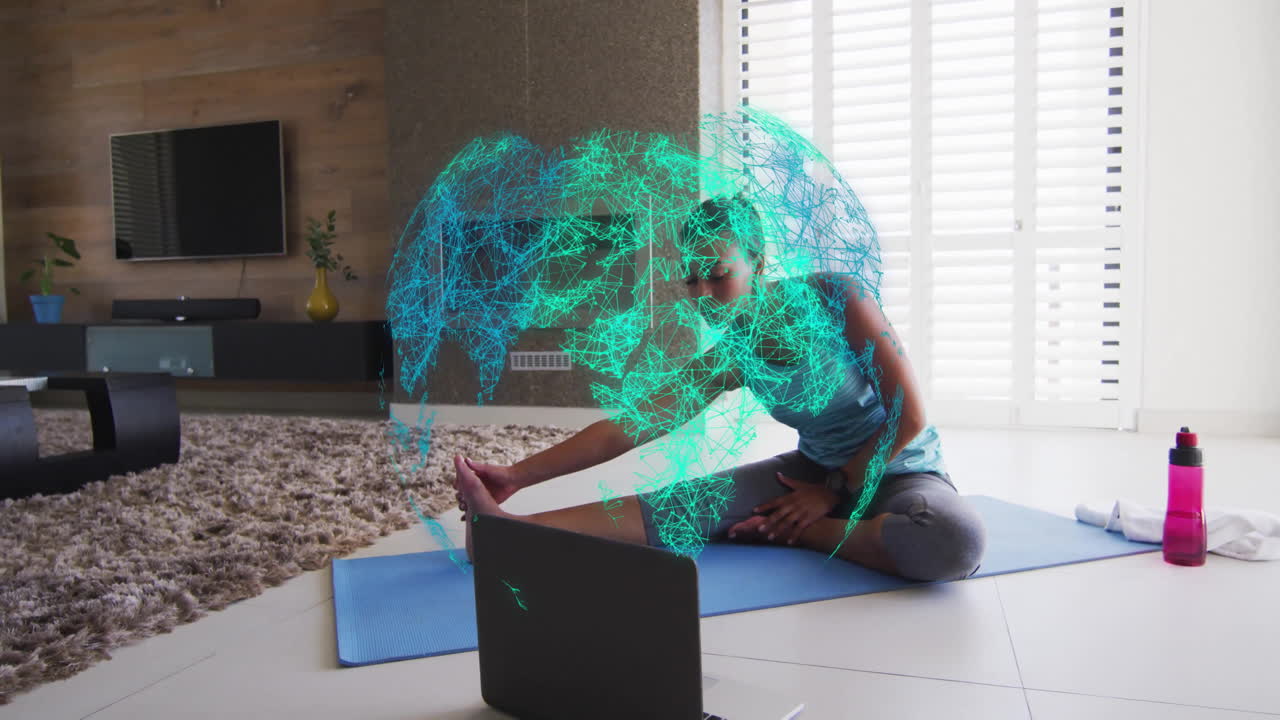 Woman stretching on yoga mat in living room, with laptop showing health data and network globe