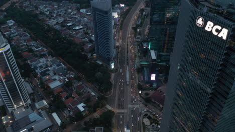 Aerial-tilting-view-following-busy-multi-lane-traffic-into-the-modern-city-with-tall-skyscrapers-in-Jakarta,-Indonesia