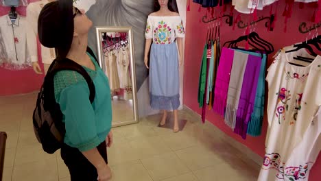 mature woman looks at a beautiful display of women’s huipil blouses in merida mexico store