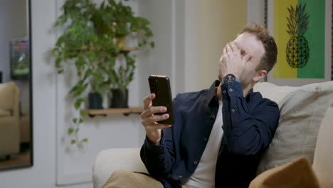 Happy-and-smiling-man-using-mobile-phone-while-relaxing-on-sofa-at-home