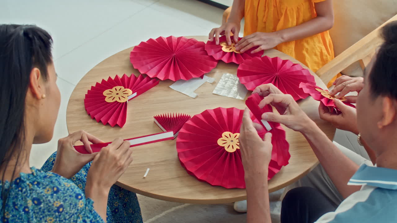 Unrecognizable Family Members Making Red Paper Decorations for Celebration