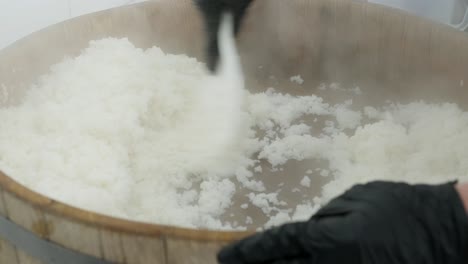 cook stirs hot rice in a wooden bowl