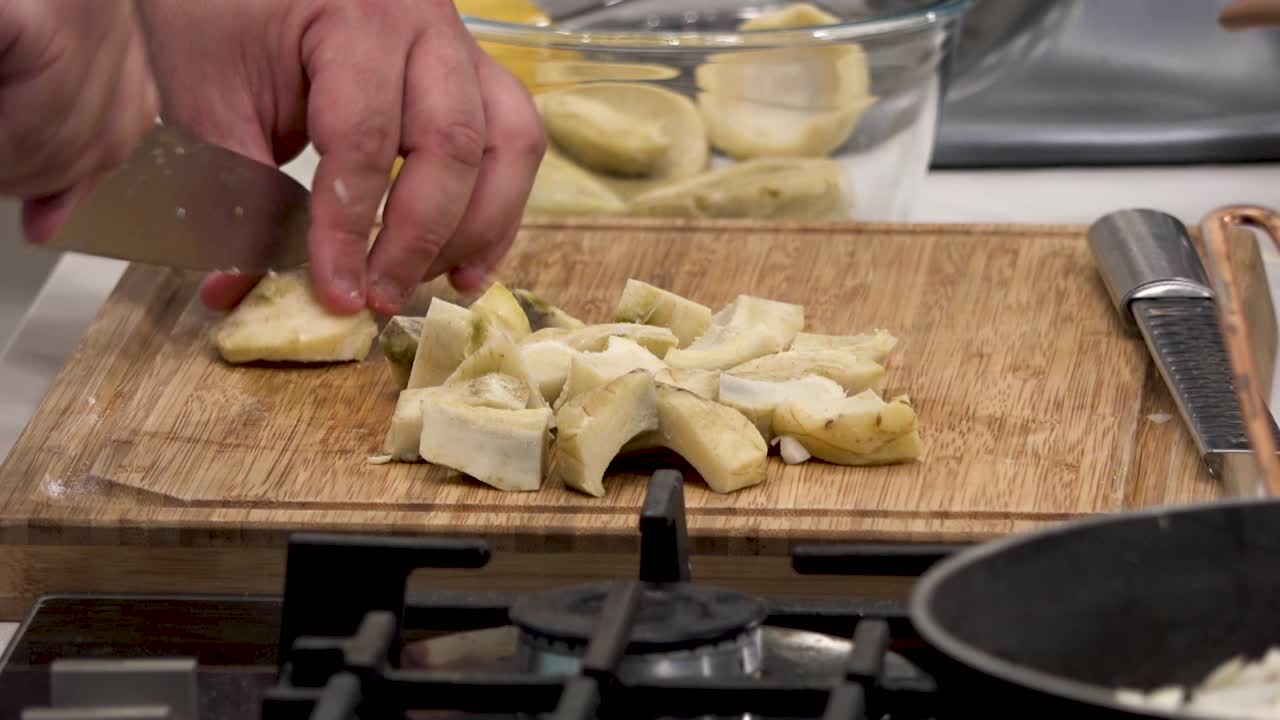 In a warm kitchen, a chef masterfully slices fresh pasta on a wooden cutting board. The preparation includes a blend of ingredients, highlighting culinary skills and kitchen ambiance