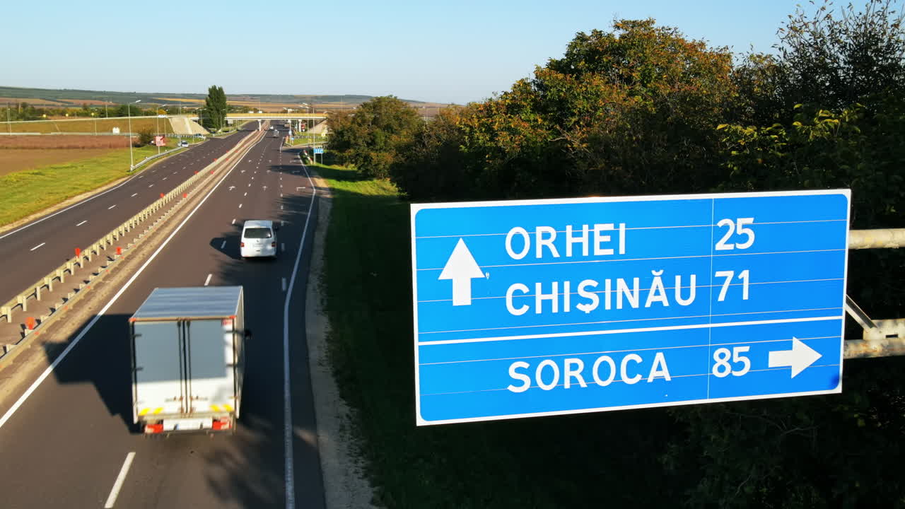 Aerial drone view of a road directions sign near a road junction with moving cars and nature around, greenery, Moldova