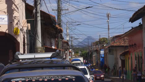 busy traffic street of leon nicaragua, cars people passing central america, volcano in the distance