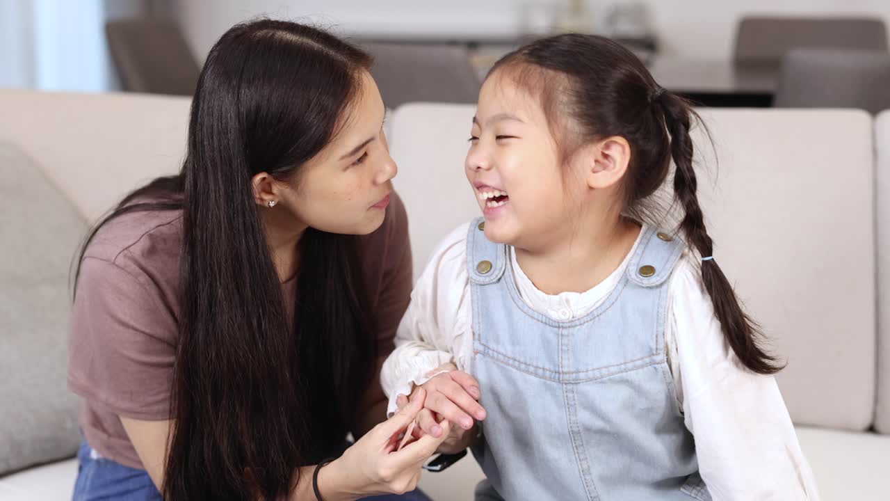 A mother and daughter share laughter on a cozy sofa, creating a warm and joyful atmosphere in a bright living room
