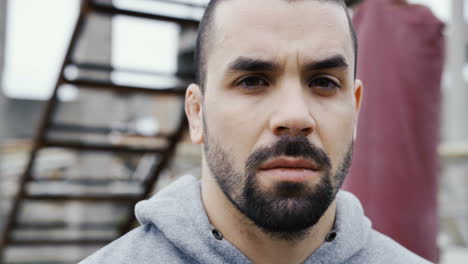 close-up view of the bearded sportsman turning and looking with serious expression at the camera outdoors an abandoned factory on a cloudy morning