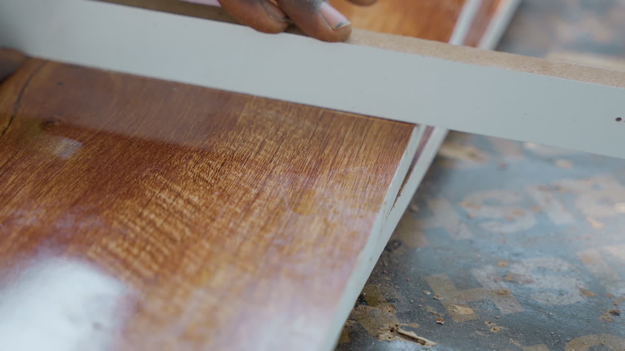 Primo piano di un falegname che leviga il bordo di un'asse, levigando una tavola di legno duro lucida su un banco con un utensile manuale, leggera spolverata di segatura e colpi deliberati e precisi che evidenziano l'artigianalità e la superficie