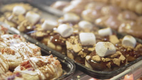 panning shot left to right of donut shop display case with large variety of sweets and flavors in warm light