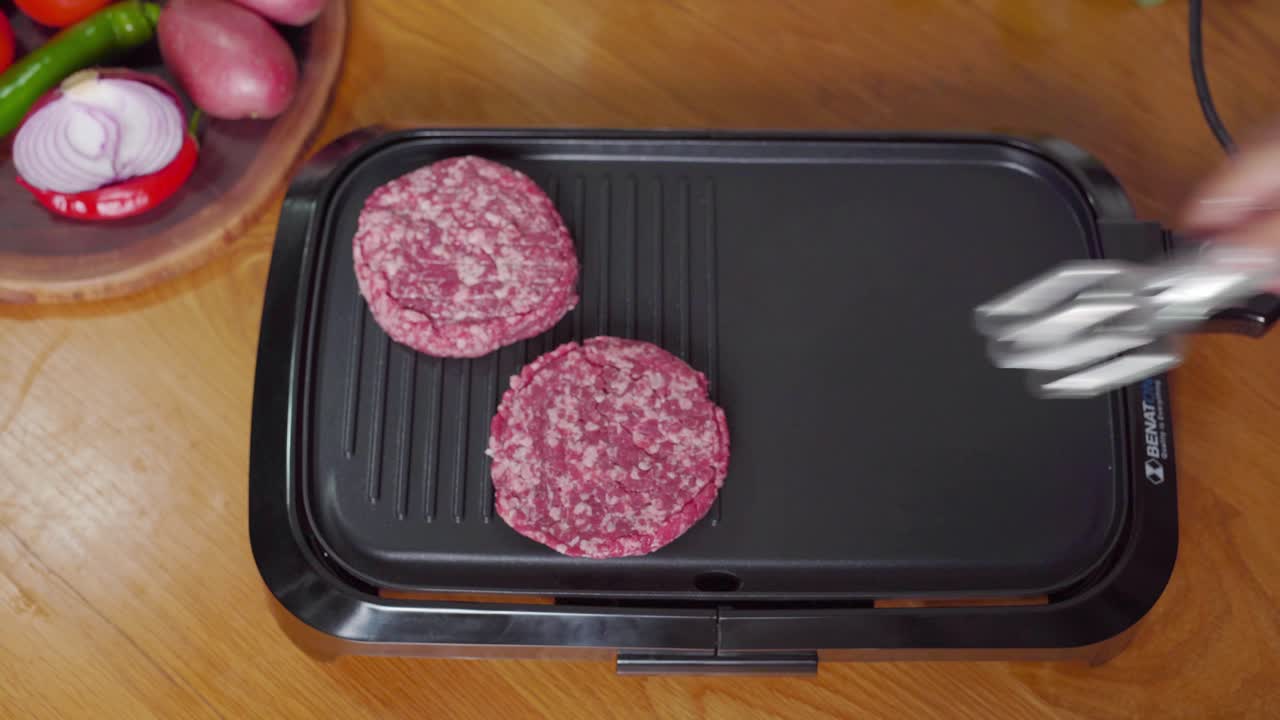 primer plano de las manos preparando una hamburguesa para una en la parrilla de la mesa, escena de la cocina