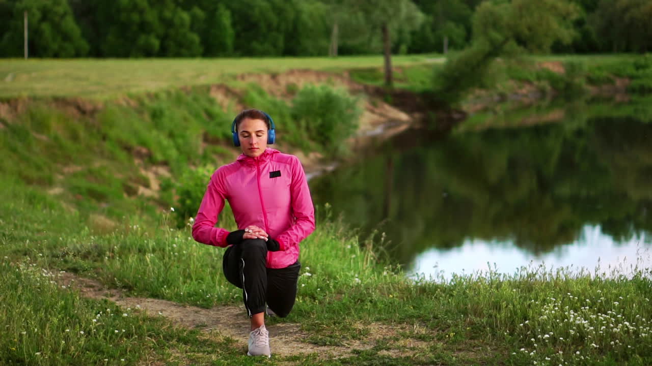 A girl in a pink jacket is preparing for a run warm up and listen to music in headphones through the phone