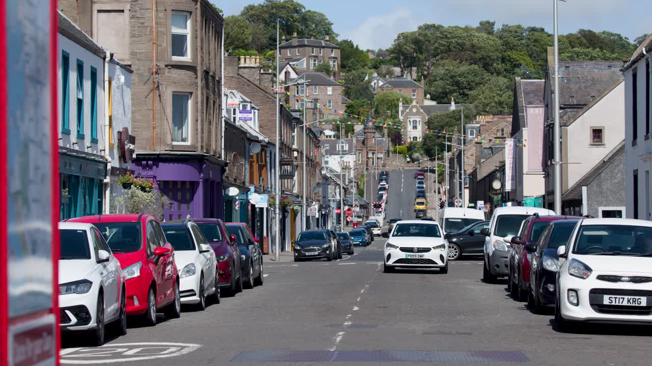 White car drives toward camera on busy Scottish street, daylight, static wide shot, urban setting