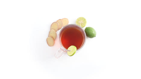 té de limón en una taza de vidrio transparente con jengibre de limón entero y en rodajas en la parte superior giratoria de fondo blanco