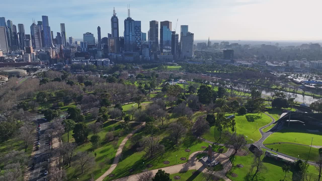 Melbourne skyline rises beyond tree filled parklands and city gardens in soft morning light