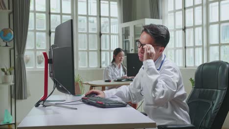 Asian Man Doctor Is Using Desktop Computer And Headache In Workplace. Medical Concept