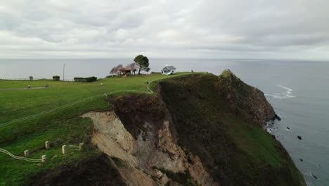 A-small-chapel,-Ermita-de-la-regalina,-and-a-horreo,-traditional-granary-from-the-north-of-Asturias-sits-in-a-steep-cliff-by-the-sea-in-the-north-coast-of-Asturias,-Spain