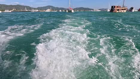 a catamaran sails through phuket's turquoise waters, leaving a foamy wake under clear skies and bright sunlight