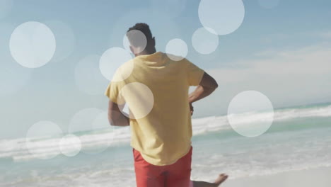 Animation-of-light-spots-over-african-american-father-and-daughter-playing-on-beach