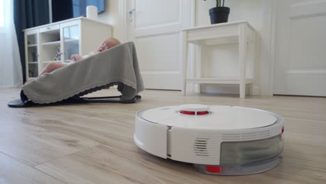 robot vacuum cleaner performs automatic cleaning of apartment moves around baby in rocking chair, modern technology of smart cleaning.
