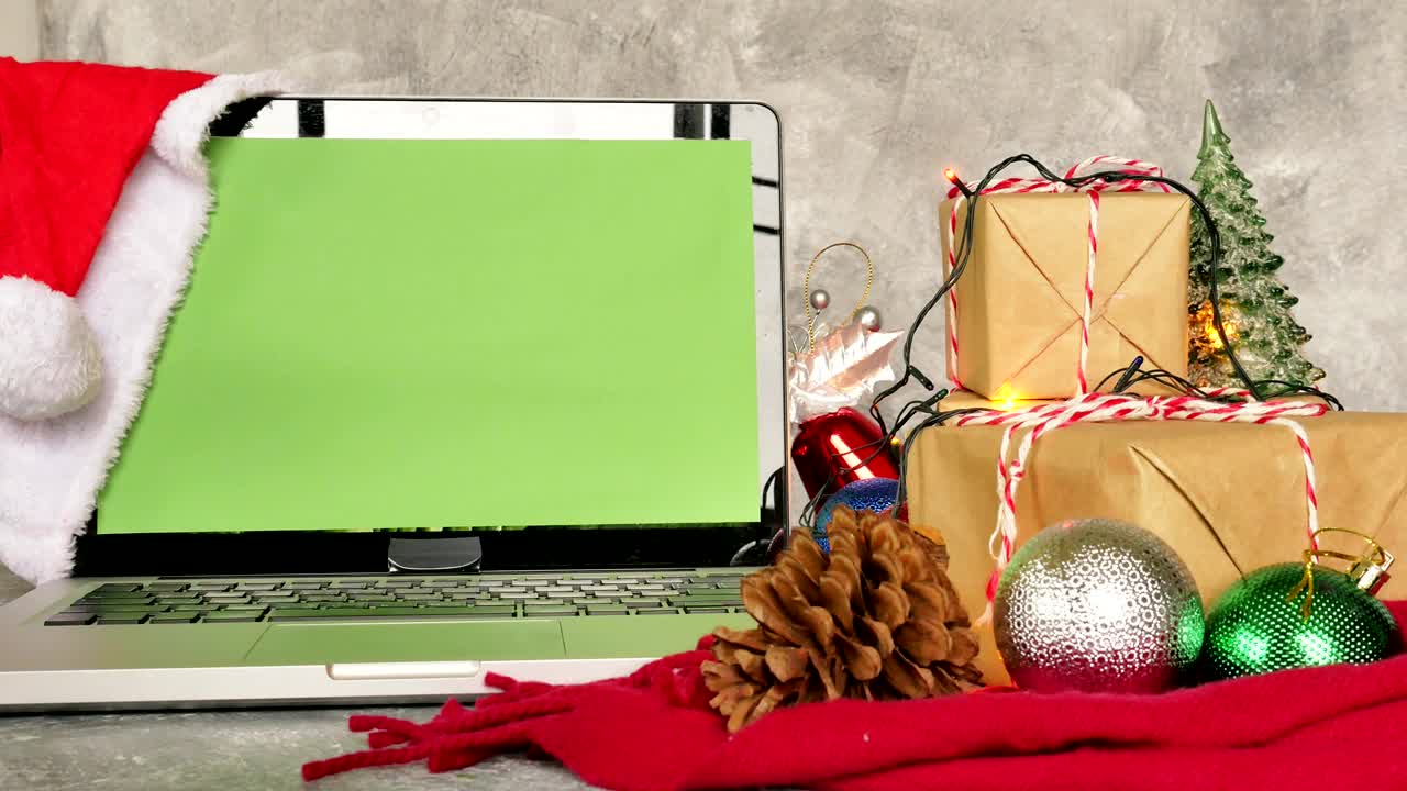 portátil con pantalla verde, cajas de regalos y decoración navideña en la mesa.