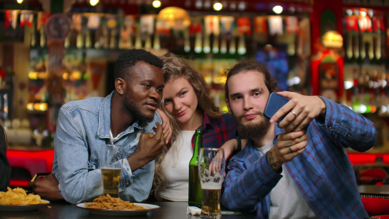 Three friends two Europeans and African American men are photographed together while sitting in a beer bar. Multinational company of friends.