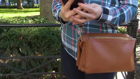 a female in a plaid shirt takes her phone out of her light brown purse and then replaces it and zips the purse