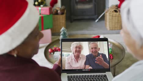 diversas amigas mayores que usan una computadora portátil para una videollamada de navidad con una pareja feliz en la pantalla