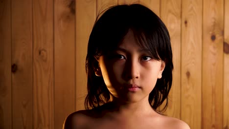 Dramatic lighting young Asian boy shirtless looking into camera on wooden background
