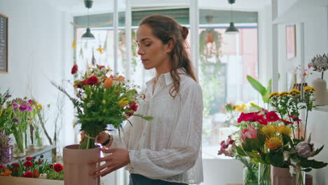 hermosa florista mira la cámara en el lugar de trabajo de la flor trabajo de la niña alegre en la tienda.
