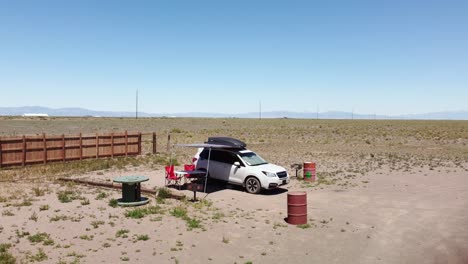 SUV-Blanco-Estacionado-En-Un-Campamento-Fuera-De-La-Red-En-El-Desierto,-órbita-Aérea