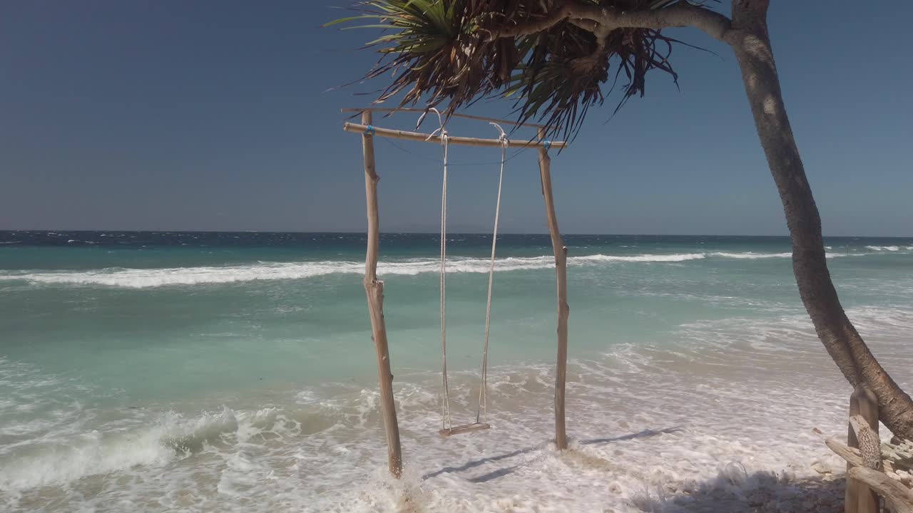 Still shot of swing on sandy beach with ocean in background. Sunny and windy evening in Bali Indonesia