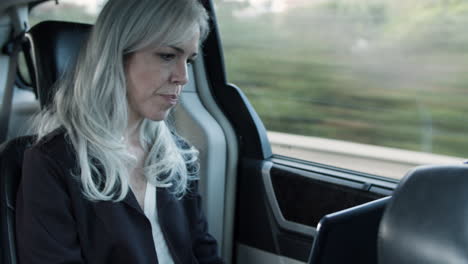 Woman-Sitting-In-Backseat-Of-Moving-Car,-Typing-On-Laptop